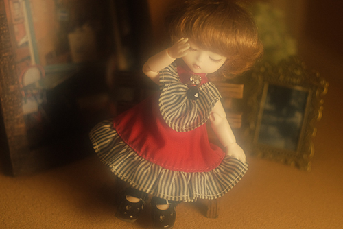 DOLL FACTORY・Baby Ariの小さな眠り目の子、Emma（エマ）。赤いドレスで、ベンチに座り、どこかおすまし顔。