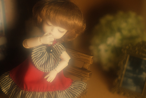 DOLL FACTORY・Baby Ariの小さな眠り目の子、Emma（エマ）。赤いドレスで、ベンチに座り、どこかおすまし顔。